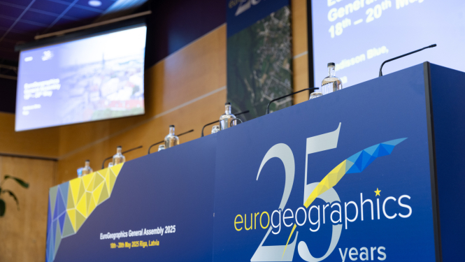 Konferences skatuve ar uzrakstu 'Eurogeographics 25 years' un ekrāniem, kas informē par EuroGeographics Ģenerālo asambleju Rīgā 2025. gadā.
