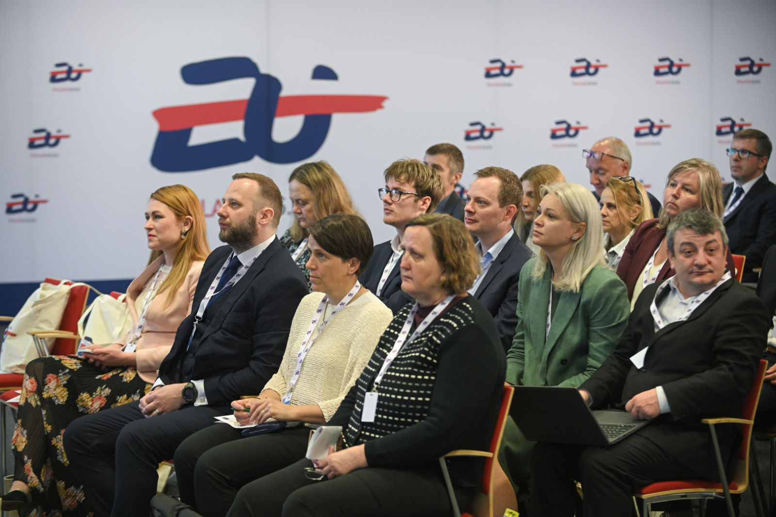 Konferences dalībnieki sēž auditorijā un klausās prezentāciju, fonā redzams pasākuma grafiskais noformējums ar Eiropas kadastra tematiku.