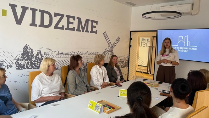 Telpā ar uzrakstu pie sienas "Vidzeme" pie galda sēž vairāki cilvēki