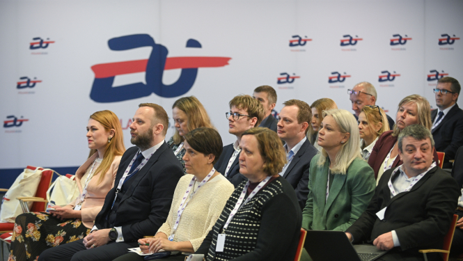 Konferences dalībnieki sēž auditorijā un klausās prezentāciju, fonā redzams pasākuma grafiskais noformējums ar Eiropas kadastra tematiku.